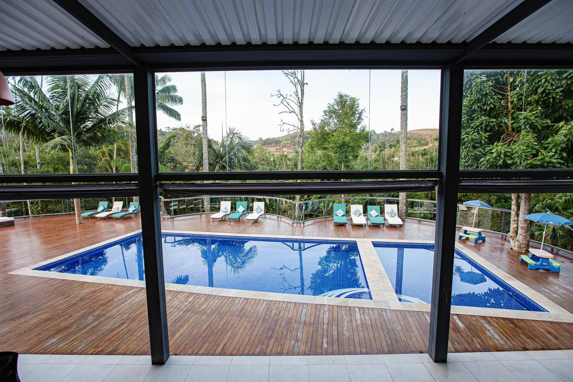 As piscinas vistas de dentro do salão coberto, com a mata ao fundo